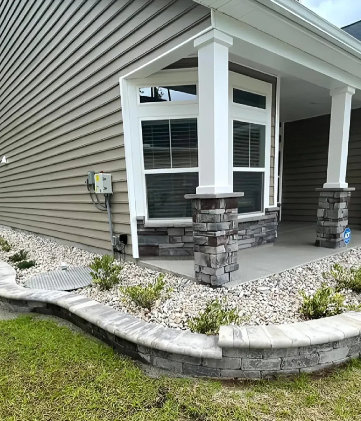 Front porch with white columns, stone bases, and curved stone retaining wall beside a tan house