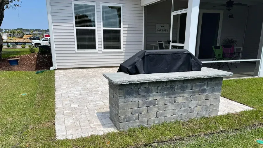 Backyard patio with a covered grill in front of a gray house and porch