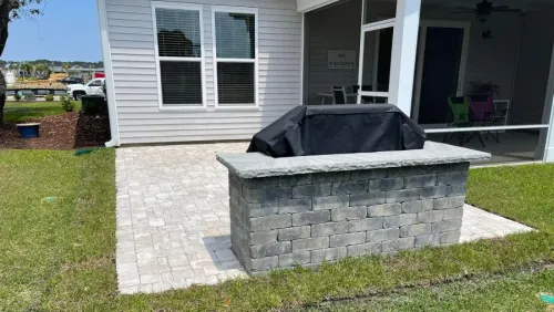Back patio with a stone fire pit in front of a house and grassy yard