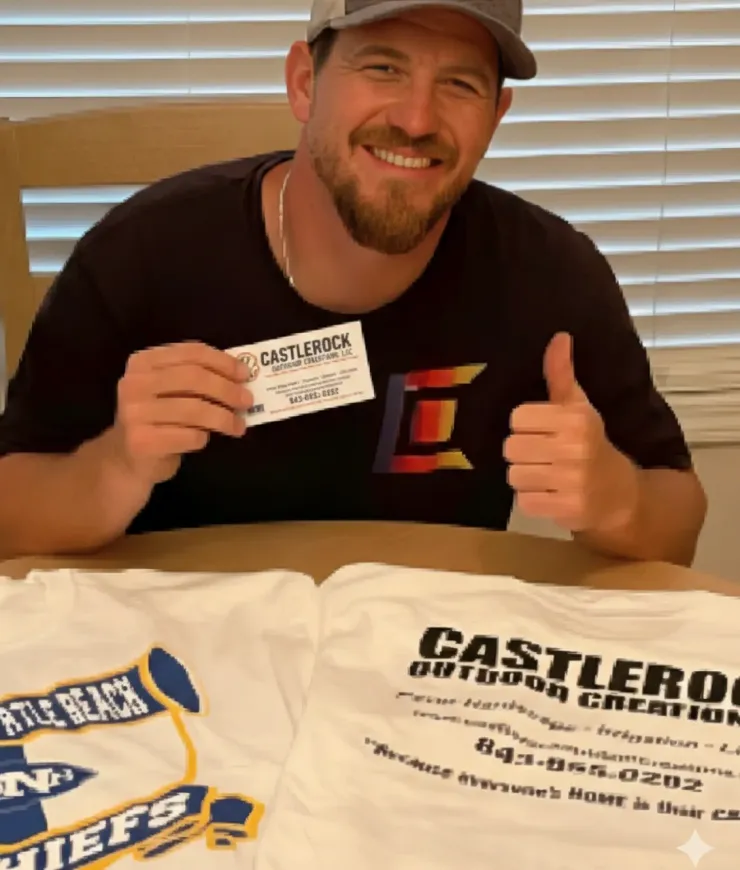 Smiling man at table holding a business card beside two printed T-shirts