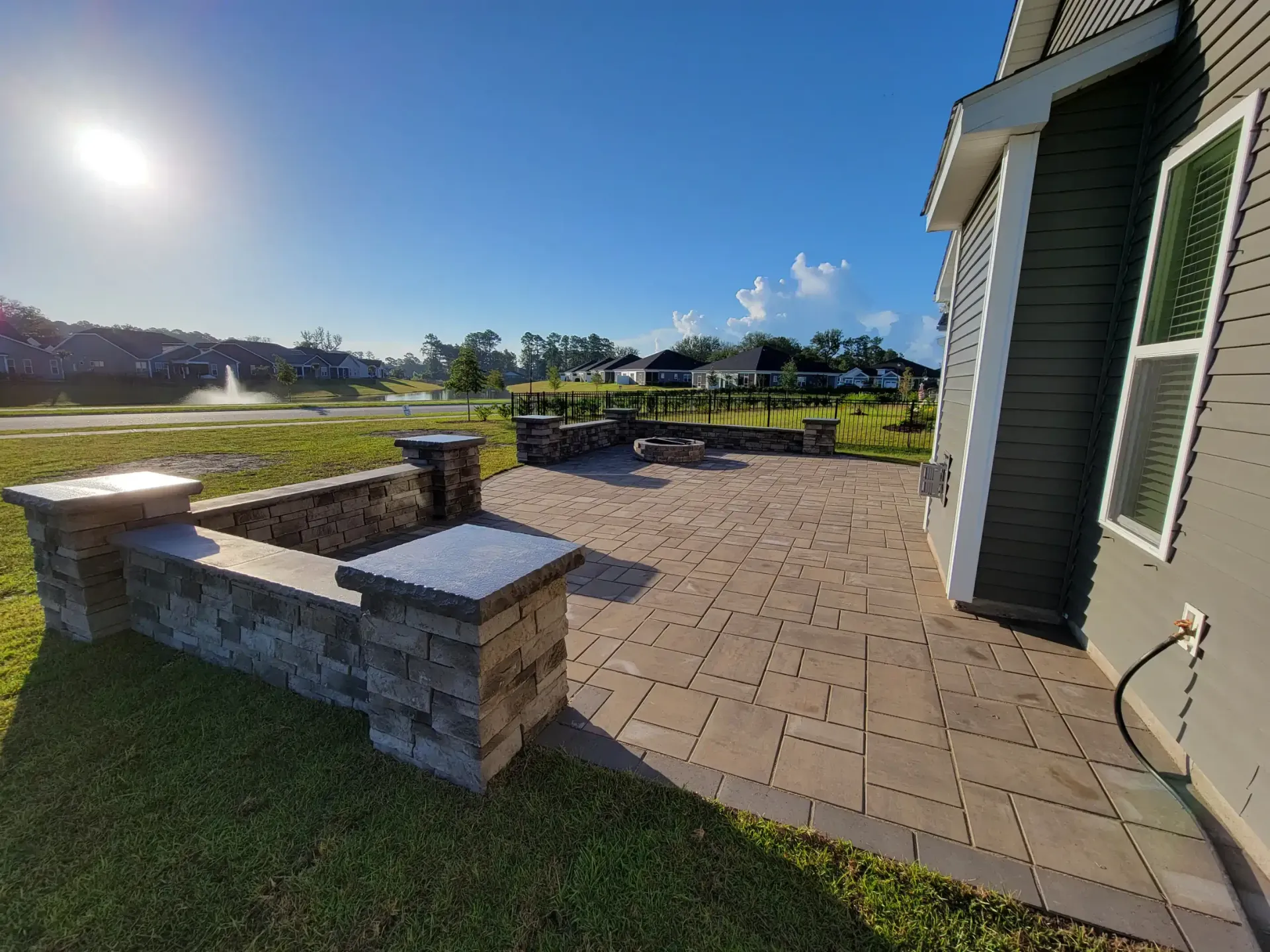 Stone patio beside a house with a grassy yard and bright blue sky