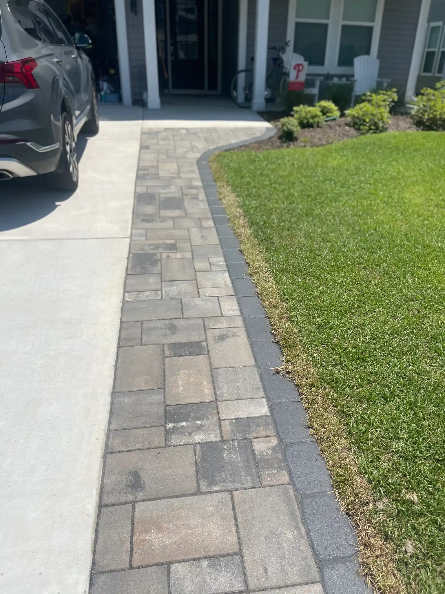 Stone walkway beside driveway leading to a front porch, bordered by lawn and landscaping.