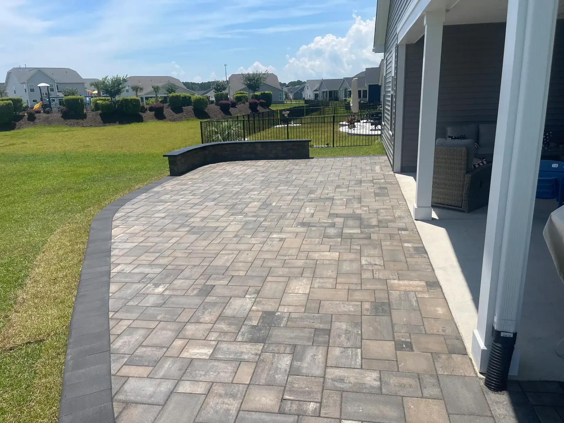 Stone-paved patio path beside a house, leading to a grassy yard under a bright blue sky.