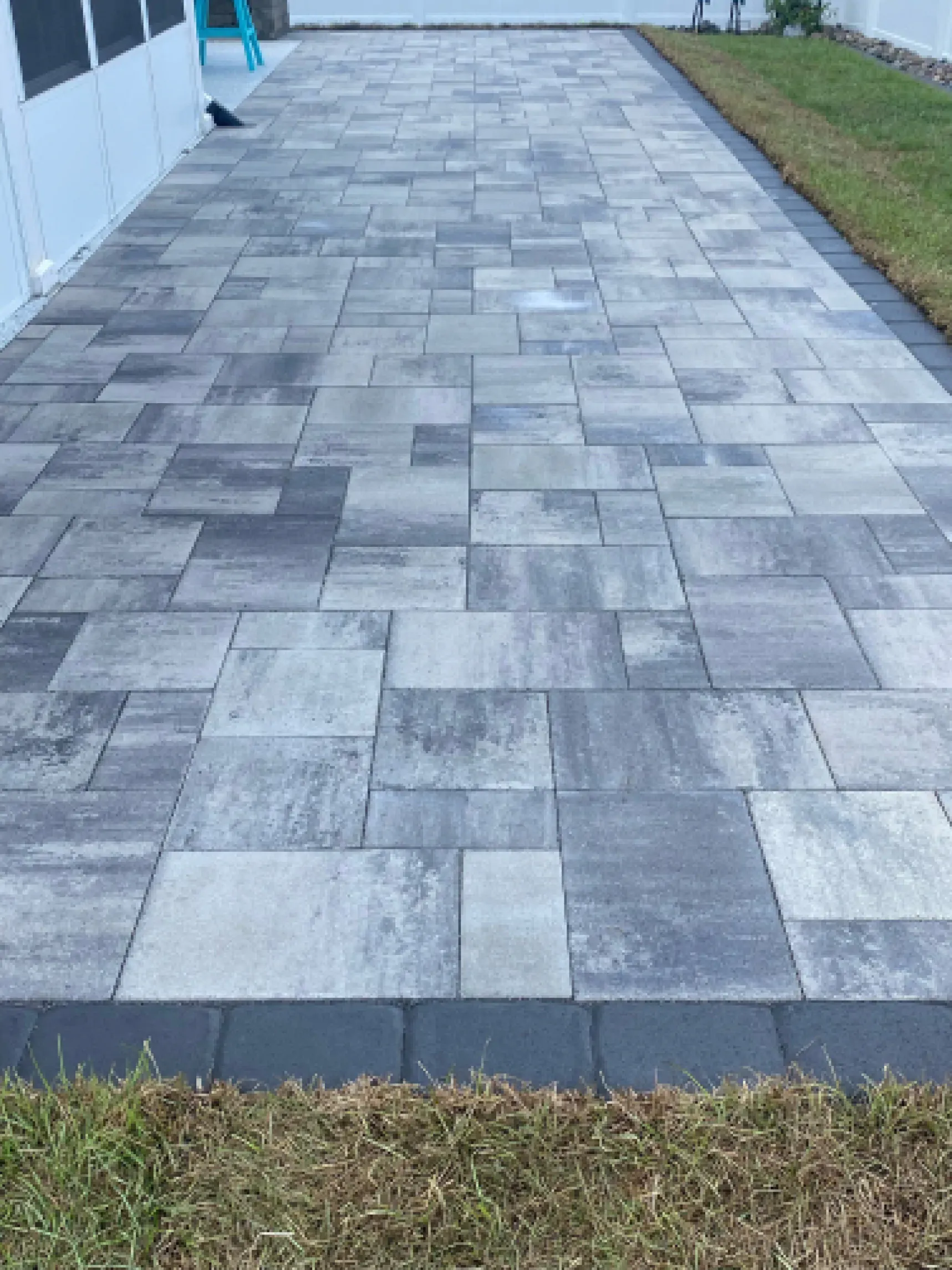 Gray tiled walkway beside a building, bordered by grass
