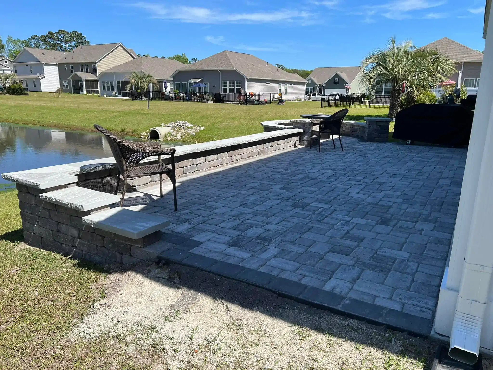 Back patio with fire pit chairs overlooking a pond and suburban homes on a sunny day