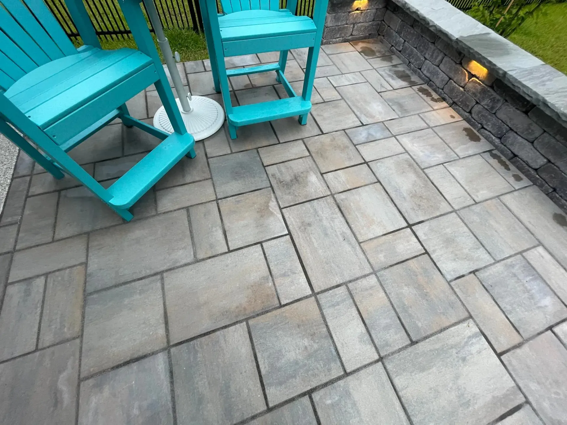 Turquoise chairs on a paved patio beside a stone planter wall and small lights.