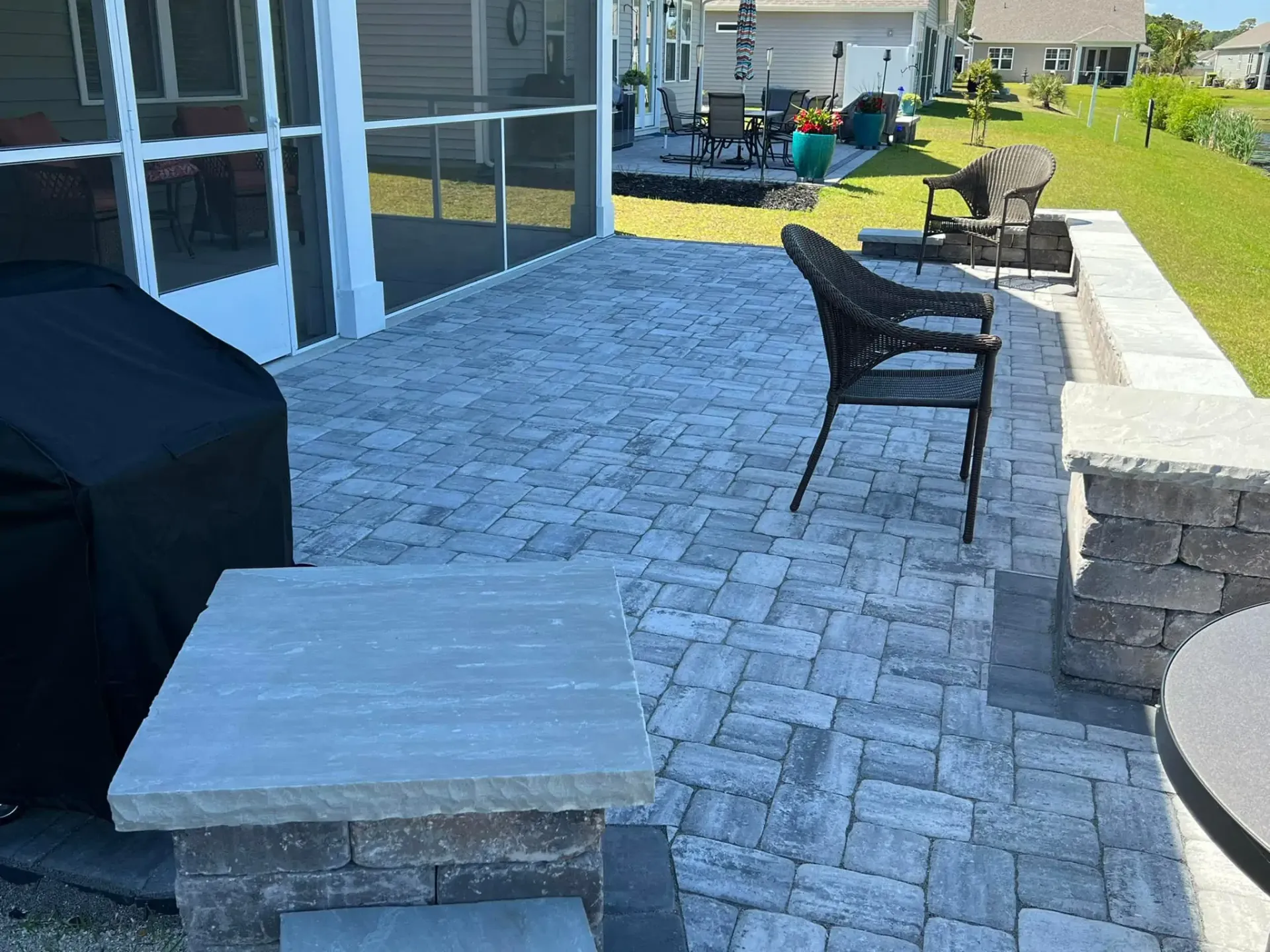 Patio with gray pavers, outdoor chairs, a covered grill, and a grassy yard beside a screened porch
