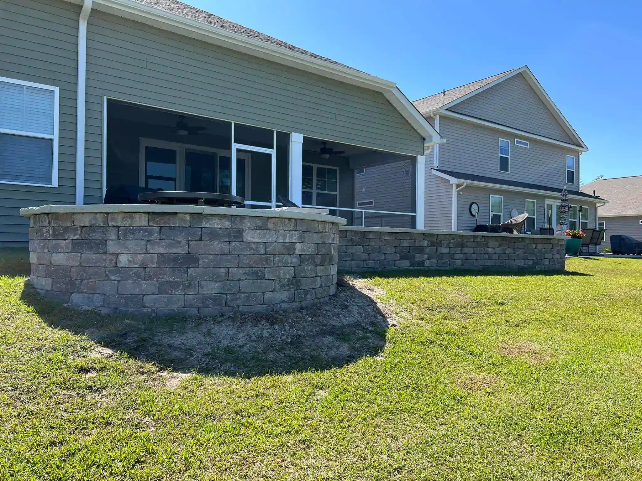 Suburban house with stone retaining wall and green lawn under a bright blue sky