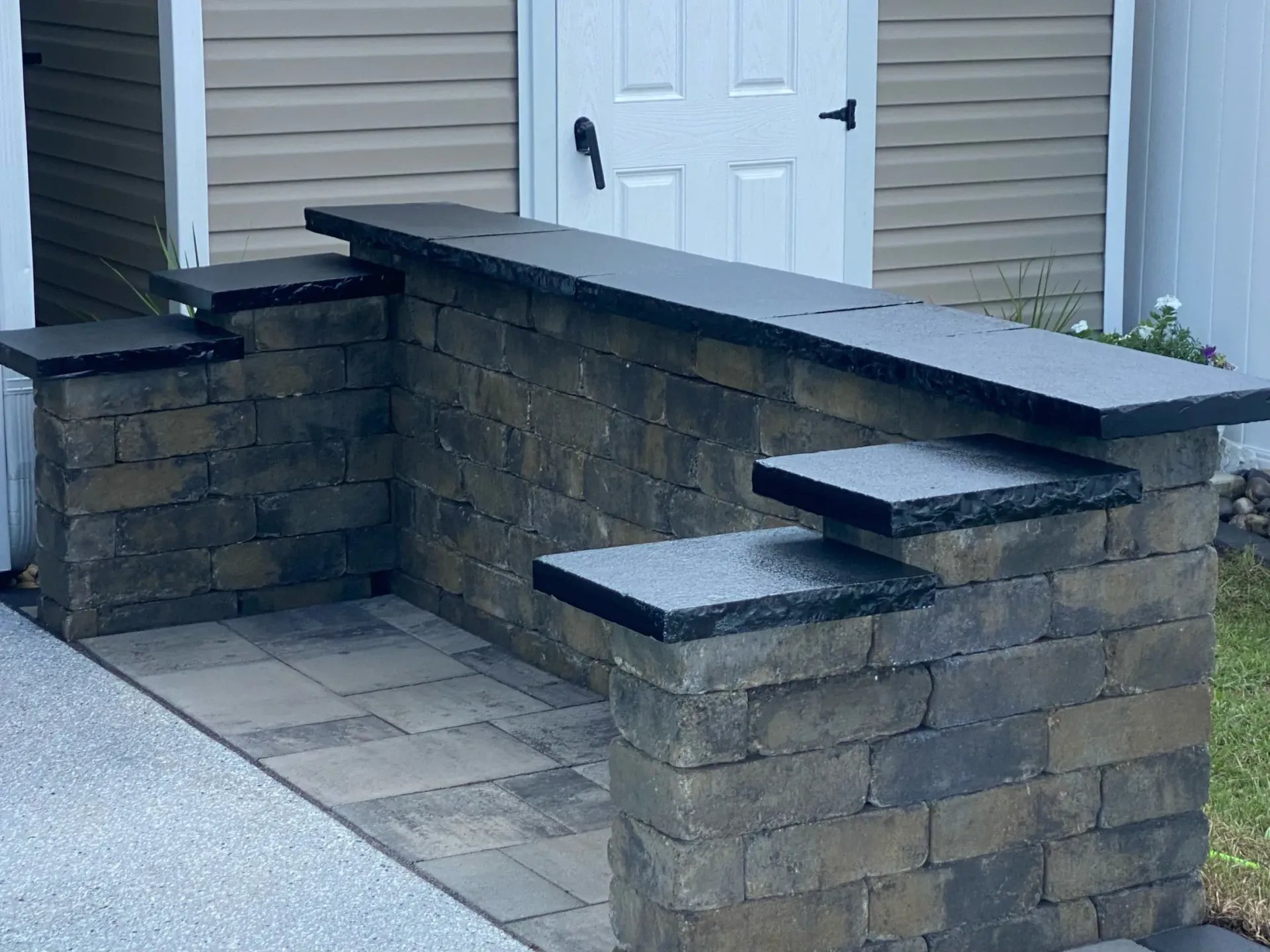 Brick planter wall and steps beside a house entrance with a white door and paved walkway