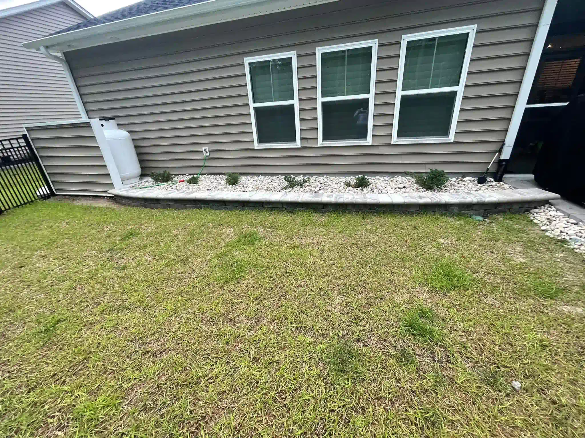 House exterior with gray siding, three windows, white rock border, and a patchy green lawn