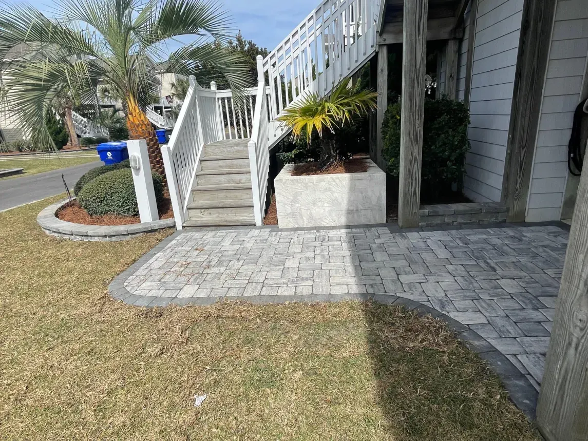 Apartment entrance with white stairs, paver walkway, and palm trees beside a lawn