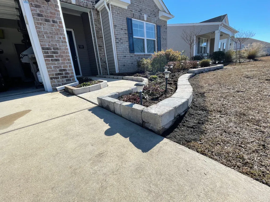 Front walkway beside a brick house with a raised stone planter and dry landscaping