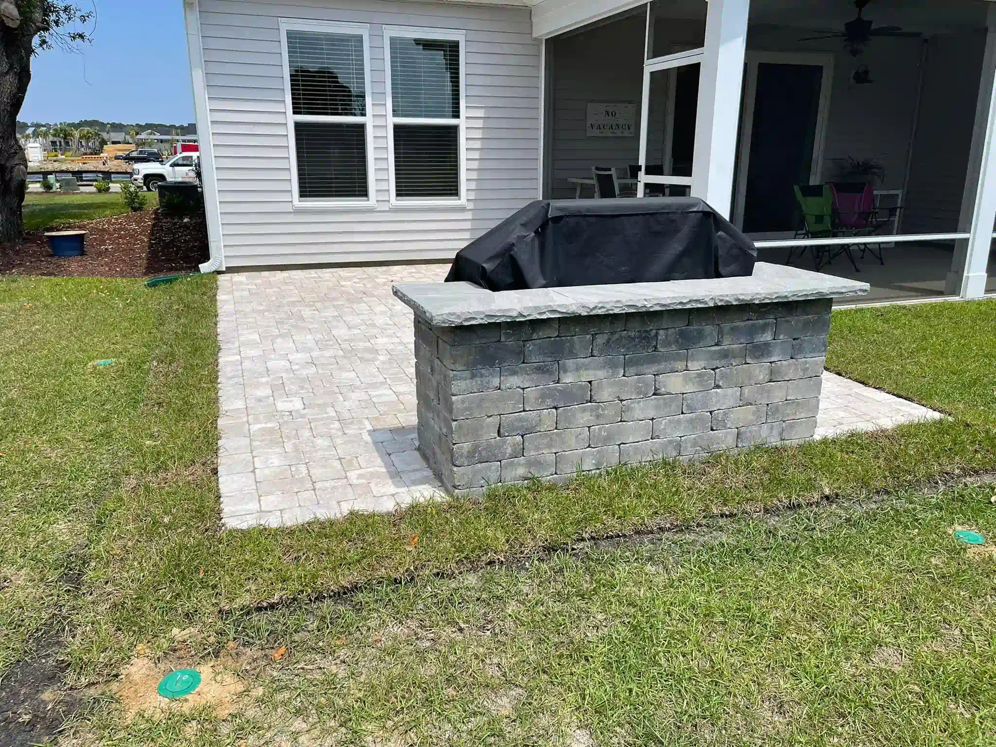 Backyard patio with a stone fire pit and a house with a covered porch and windows.