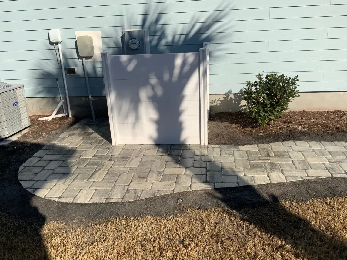 Backyard patio with pavers, a large planter, and a small shrub against a house wall