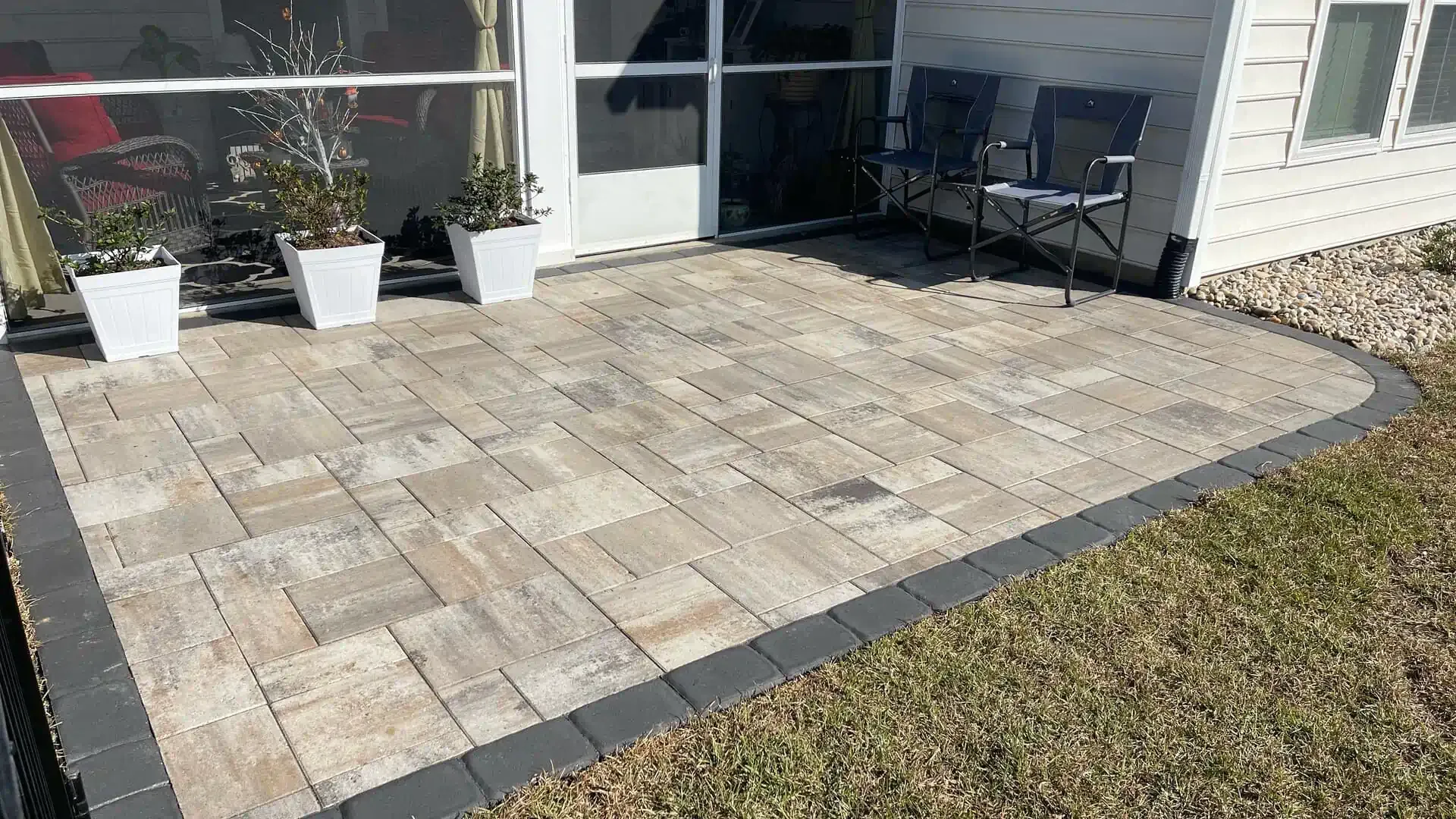 Patio with light stone pavers, gray border, potted plants, and outdoor seating beside a house