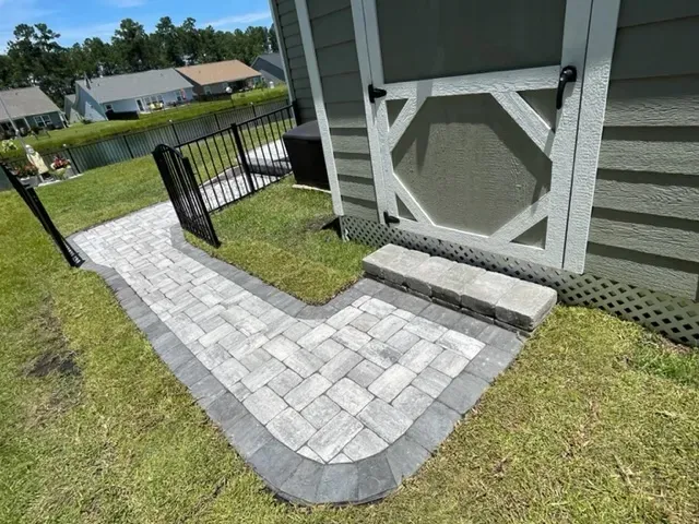 Brick walkway to a screened porch with a short step and black gate in a grassy yard