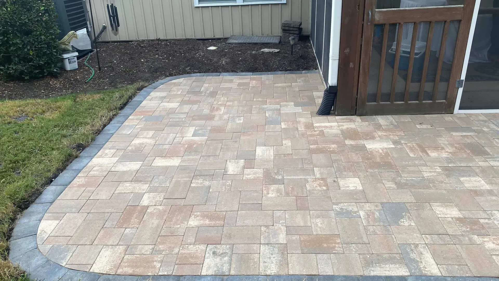 Paver patio beside a house with a small wooden gate and a grassy yard
