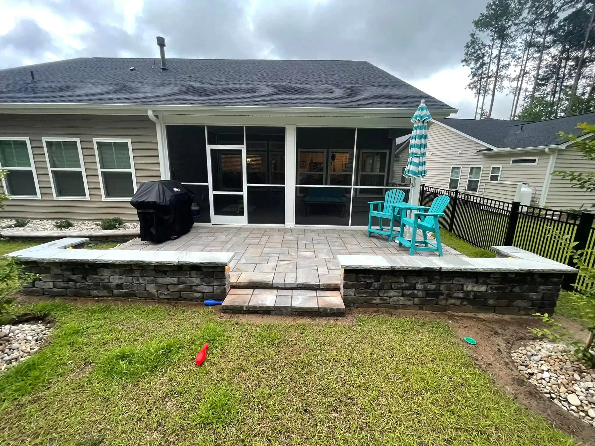Backyard patio with a raised deck, sliding doors, grill, and turquoise chair beneath a cloudy sky