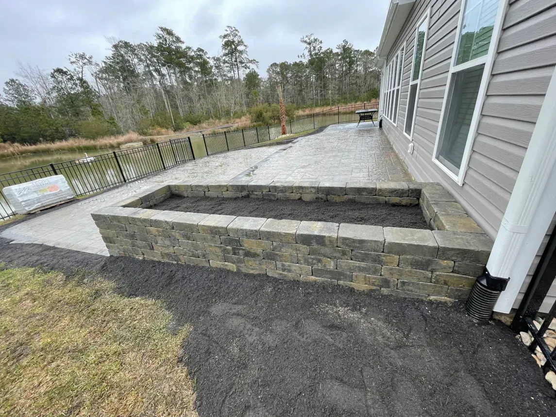 Stone steps and a gravel patio beside a house, with a fenced yard and trees beyond.