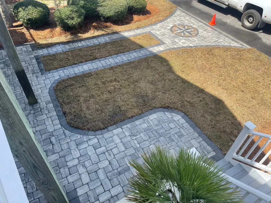 Landscaped courtyard with pavers, mulch beds, shrubs, a small palm, and a parked truck nearby