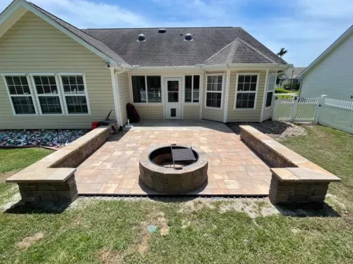 Backyard patio with stone pavers, circular fire pit, and built-in benches beside a house