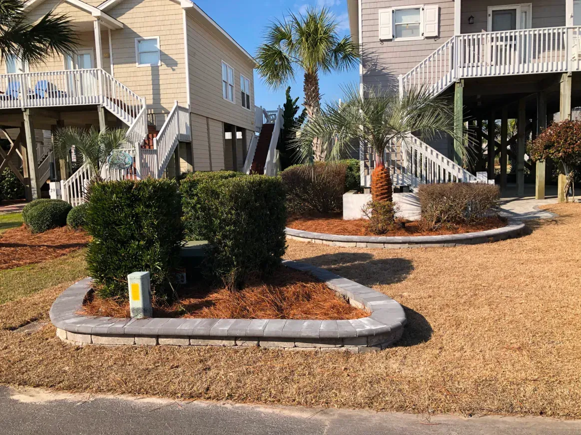 Apartment courtyard with manicured hedges, palm trees, and raised white garden beds under a bright sky