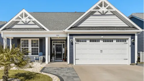 Single-story suburban house with blue siding, white trim, and a two-car garage under a clear sky.