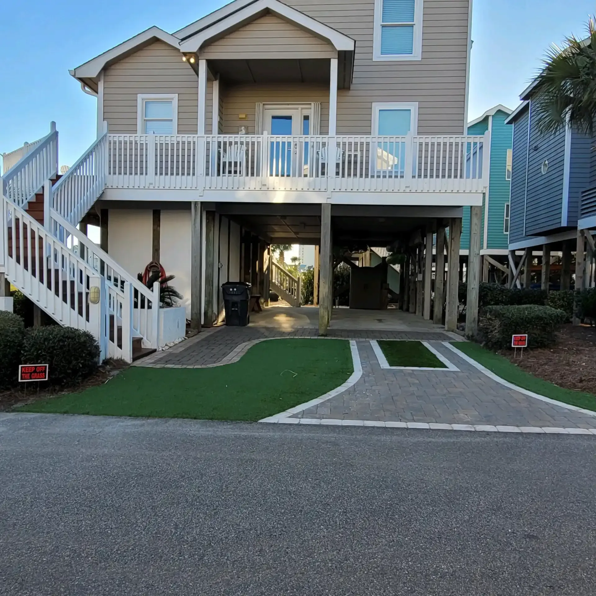 Raised beach house with white deck, stairs, and carport over a curved driveway by the road
