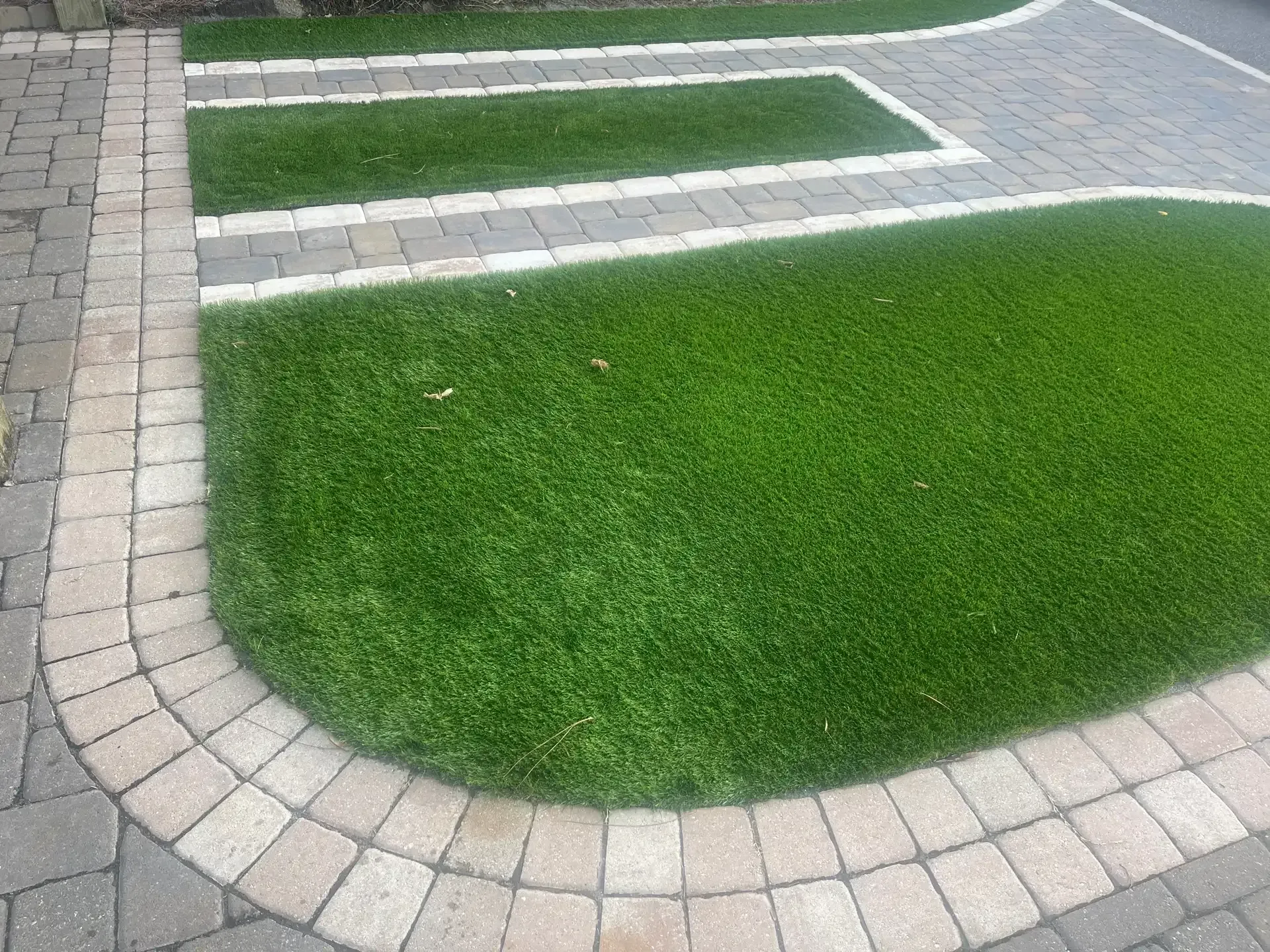 Curved stone walkway bordering a bright green lawn and landscaped grass area.