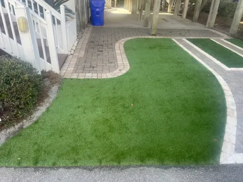 Green lawn bordered by a curved white path beside a brick walkway and blue trash bin outdoors
