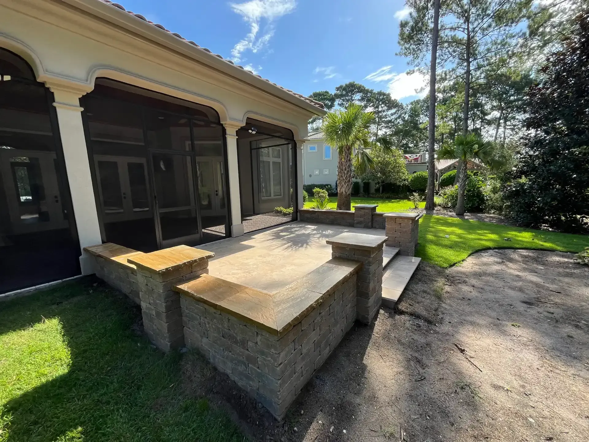 Concrete steps and ramp beside a house’s garage, with a grassy yard and gravel driveway.
