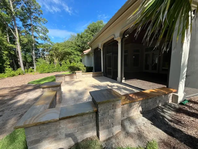Stone patio beside a house with screened porch, surrounded by trees and tropical greenery