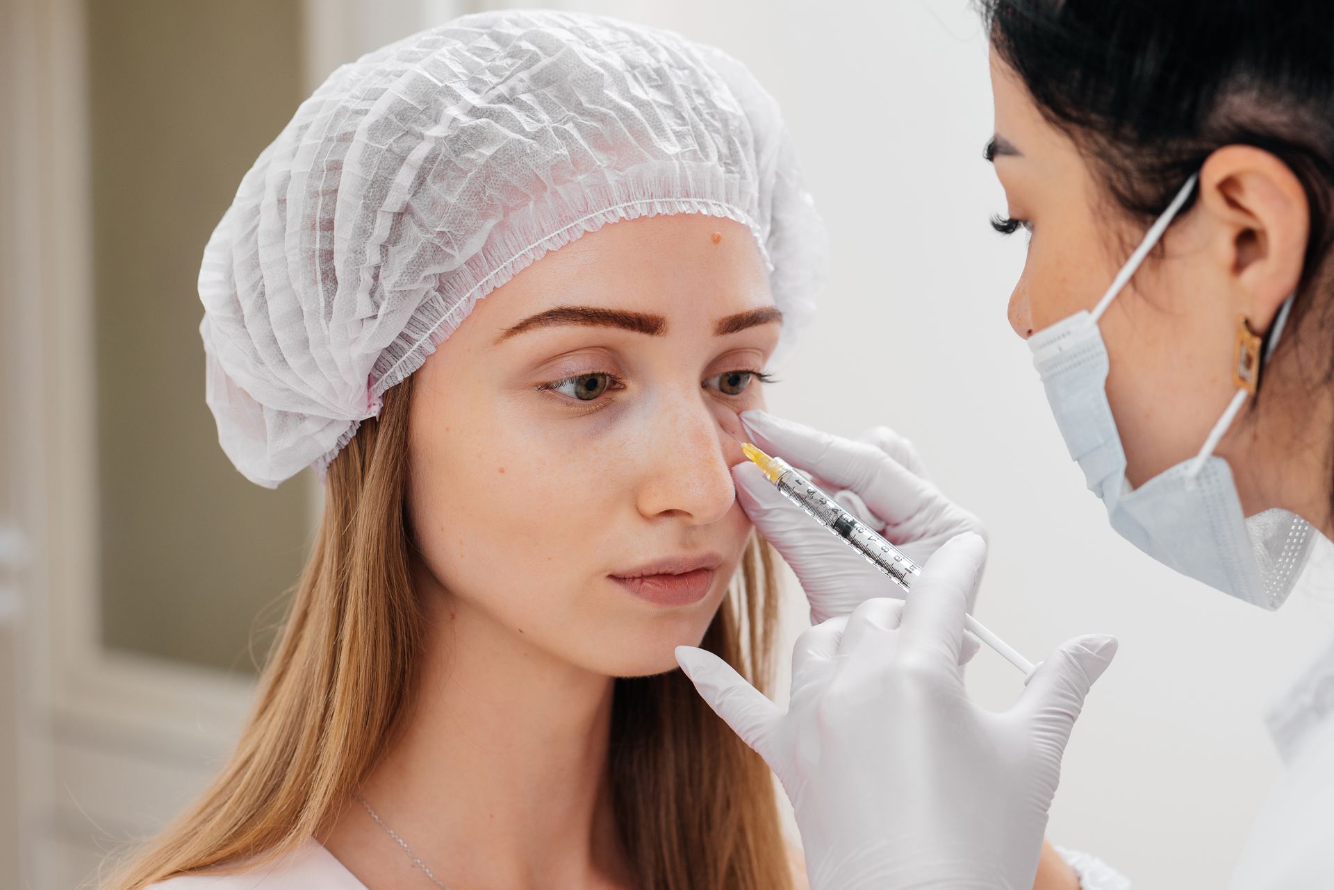A clinician examines a woman's nose with a gloved hand in a medical office.