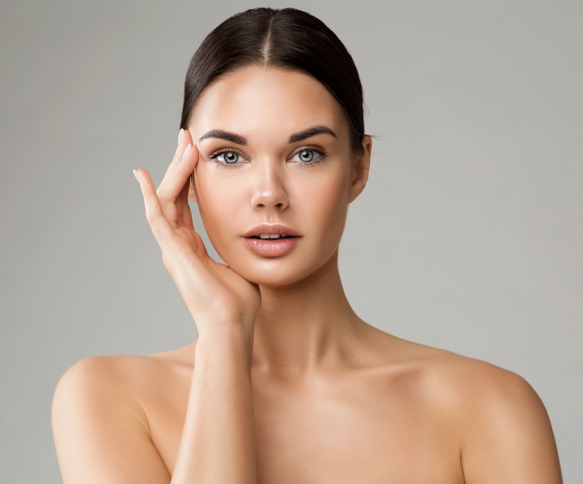Woman with fair skin, touching her face, against a neutral background.