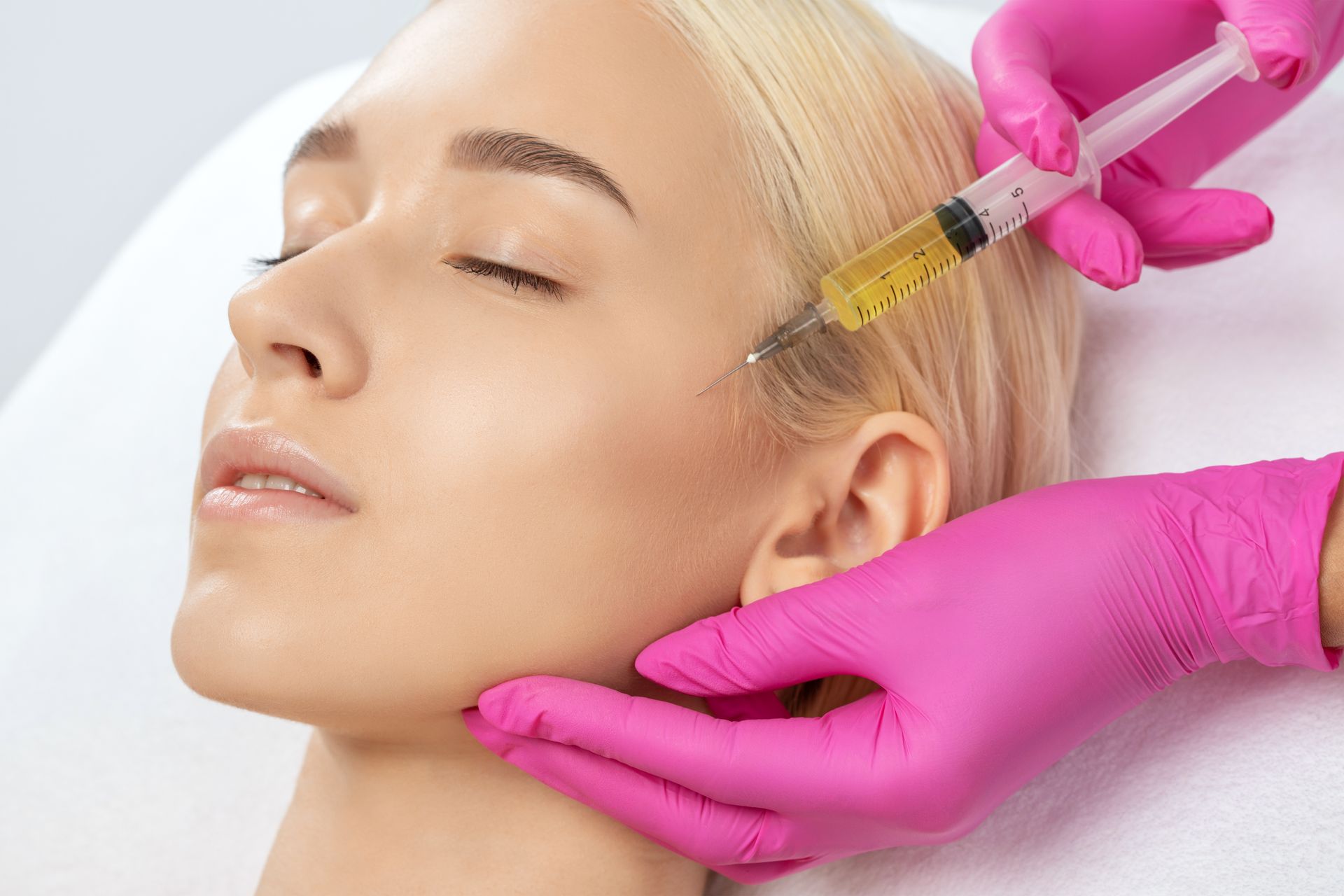 Gloved hands injecting facial treatment into a woman’s cheek while she lies with eyes closed