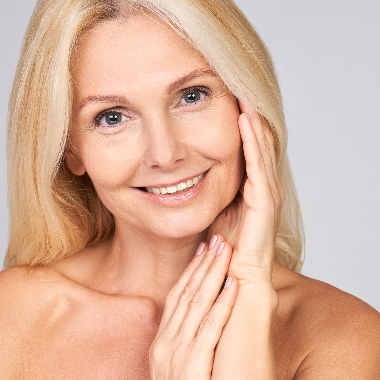 Smiling blonde person with hands on face against a light background