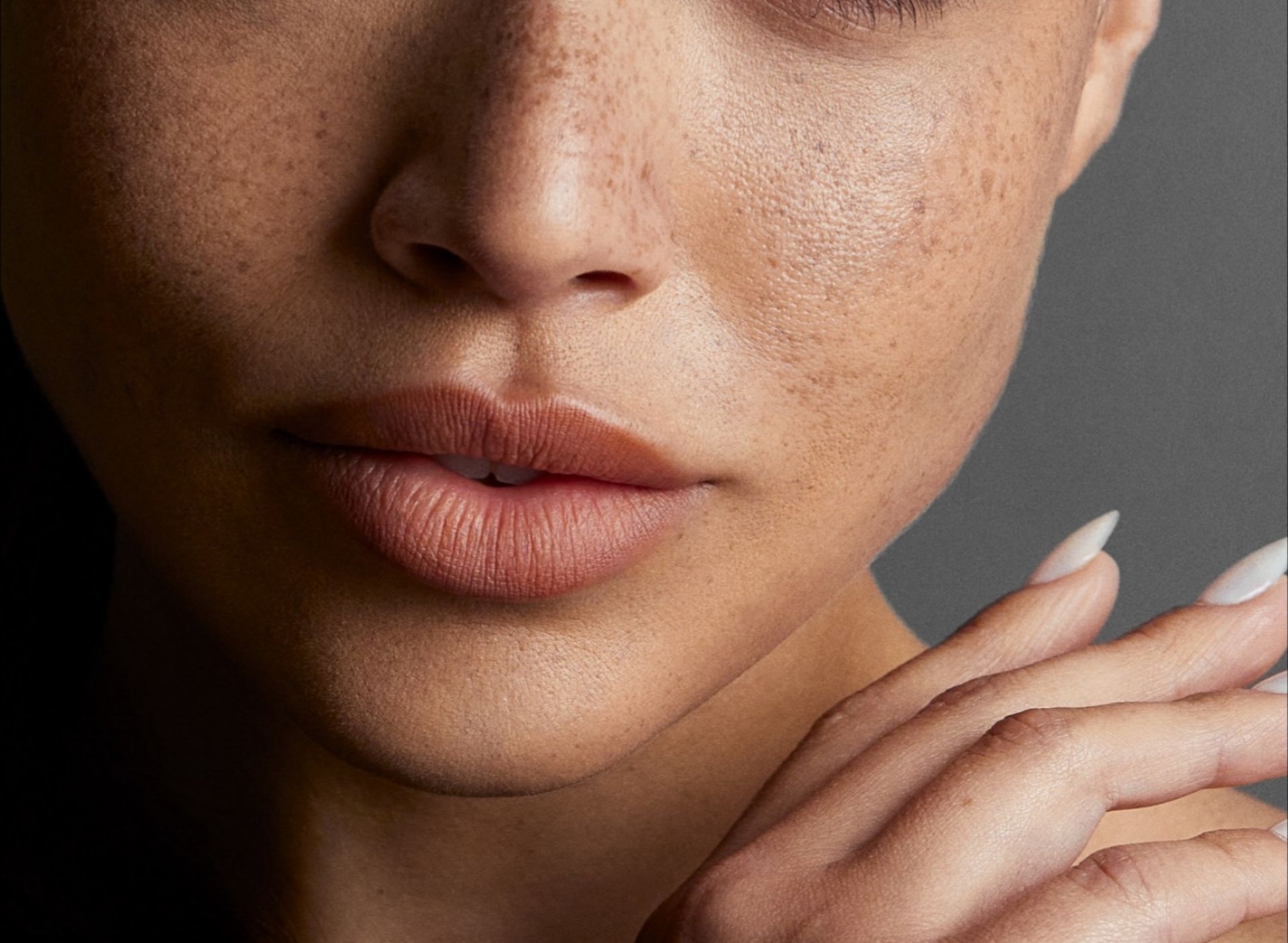 Close-up of a person's face with numerous freckles on the skin. A hand gently touches the face.