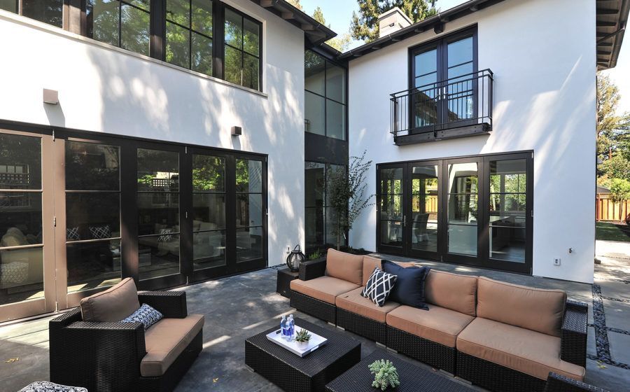Modern two-story white house with large black-framed windows and a patio with outdoor sectional seating
