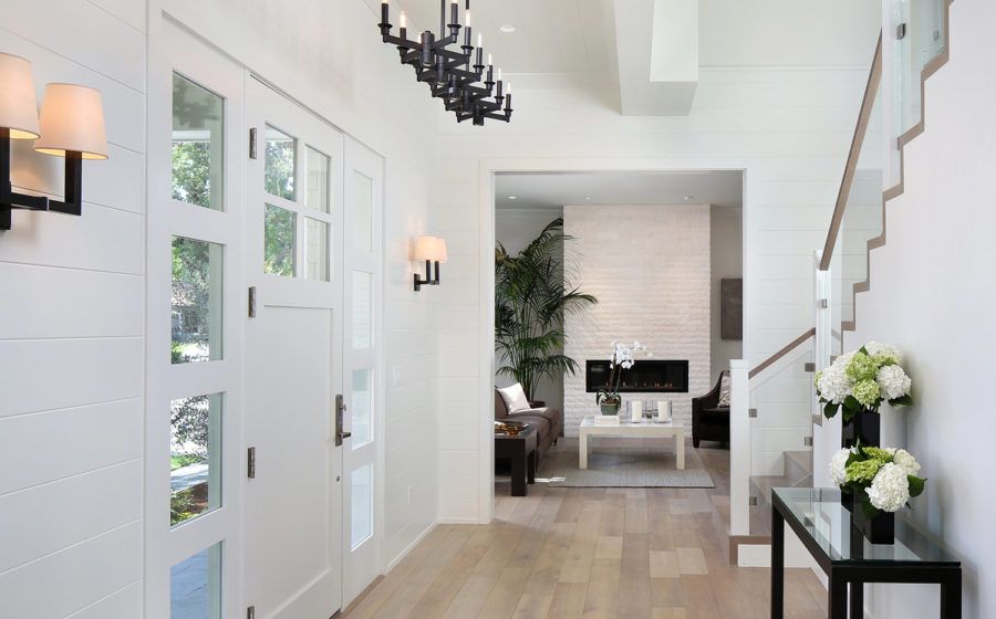 Bright entryway with white walls, light wood floor, staircase, and modern black accents