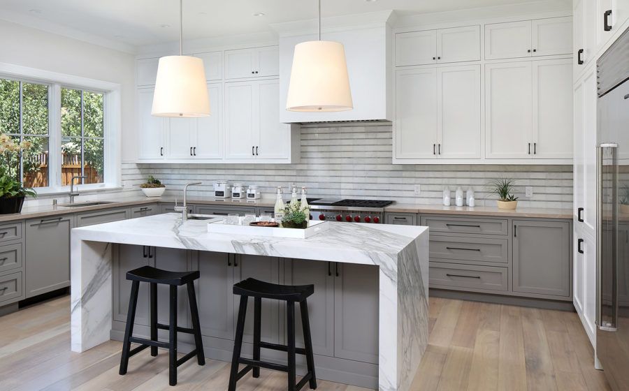 Bright modern kitchen with white cabinets, marble island, and two black stools under pendant lights