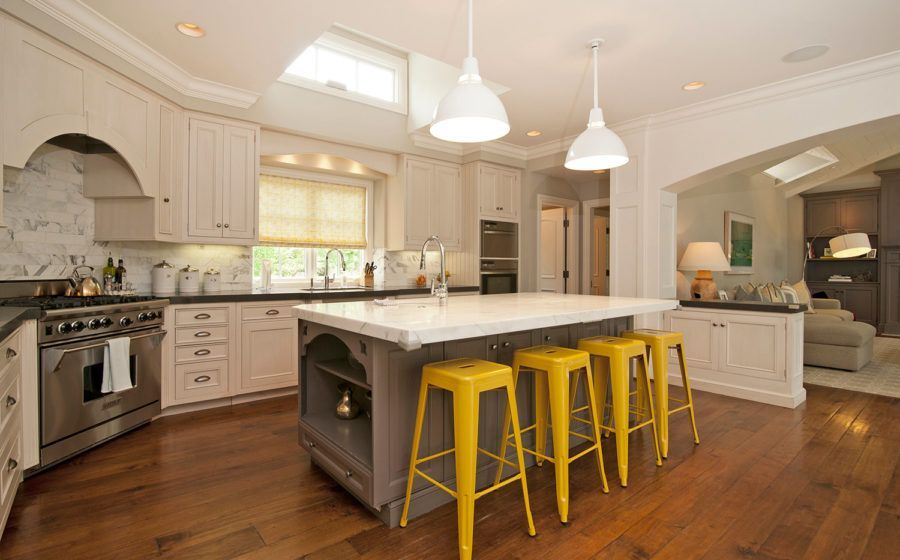 Bright modern kitchen with white cabinets, marble island, and three yellow stools on wood floors