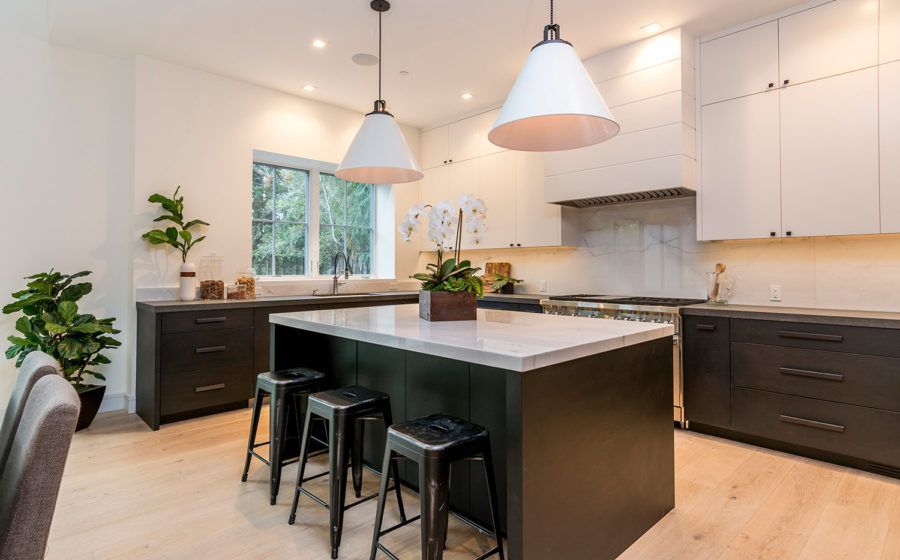 Bright modern kitchen with white cabinets, dark island, pendant lights, and stools by the counter