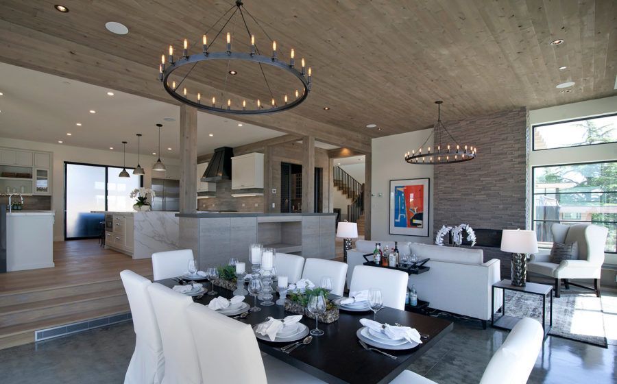 Modern open-plan living room with white sofas, dining table, and large windows under a wooden ceiling