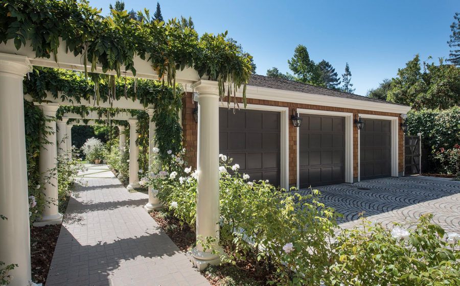 Sunlit courtyard with ivy-covered archway and a modern garage beside a gravel driveway