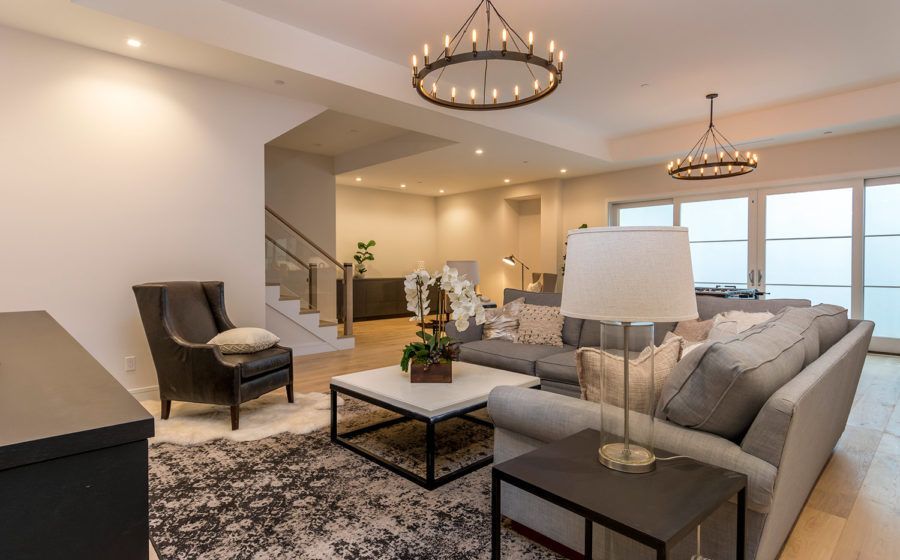 Spacious modern living room with gray sectional, chairs, coffee table, chandelier, and ocean-view windows