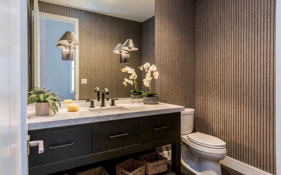 Modern bathroom vanity with double sink, large mirror, wall lights, and a toilet beside striped wallpaper