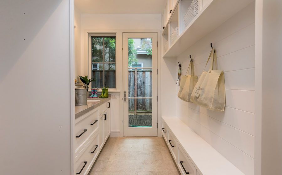 Bright narrow hallway with white cabinets, wall hooks, and a glass door opening to a small outdoor space.