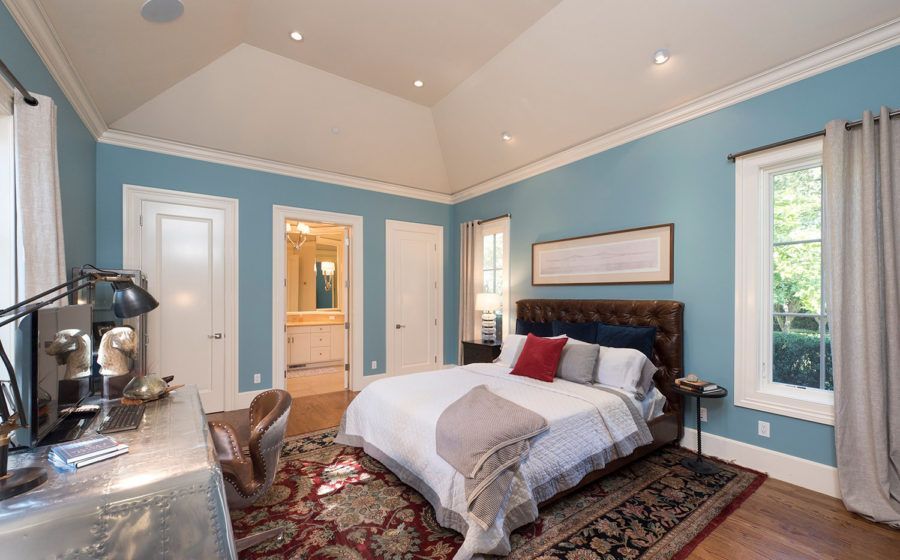 Blue bedroom with king bed, desk, patterned rug, and bathroom doorway