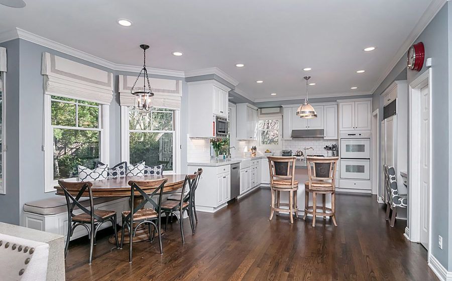 Bright open kitchen and dining area with hardwood floors, white cabinets, and a round table by large windows