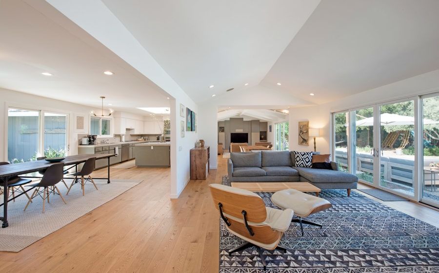 Bright open-plan living room with sectional sofa, dining area, and kitchen, featuring large windows and wood floors